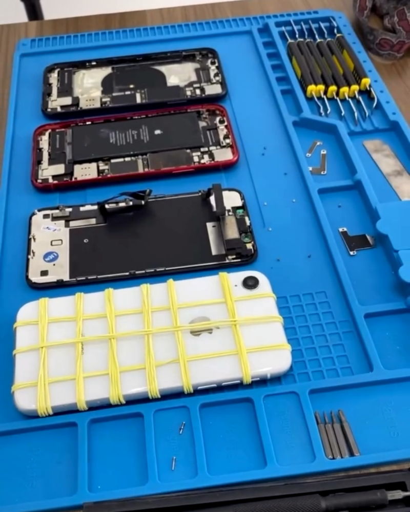 Bancada de reparo da WN com iPhones abertos, peças e ferramentas de precisão