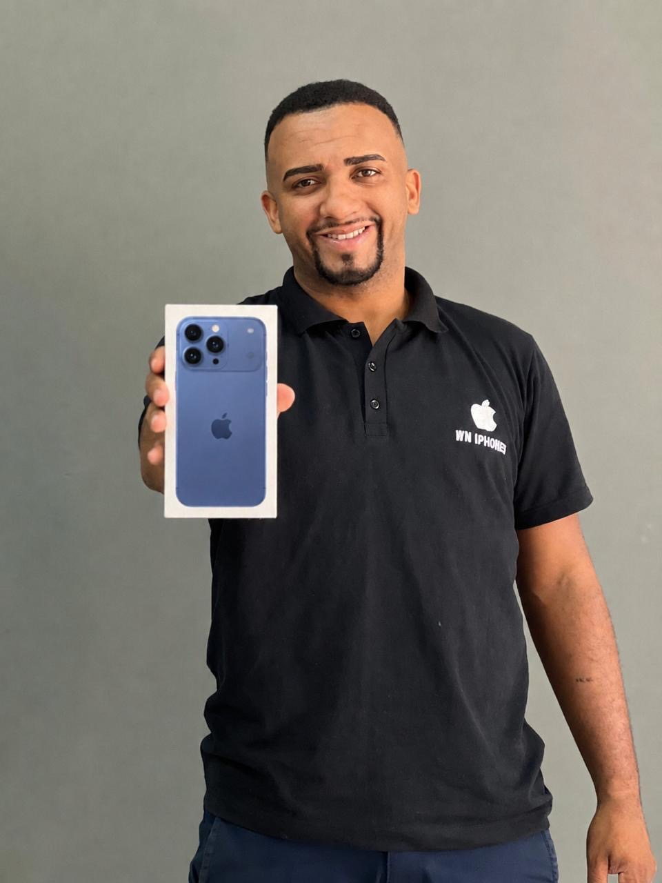 Proprietário da WN iPhones, de camisa da loja, segurando um iPhone lacrado na caixa